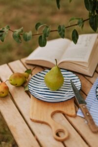 A plate with a pear on it next to a knife and a book